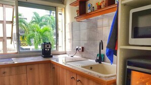 A kitchen with wooden cabinets, a sink, a coffee maker, and a stove. - Apartment by the sea (Le Gosier)