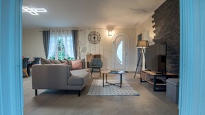 Een moderne woonkamer met een grijze bank, een klein tafeltje, een tv-meubel en een decoratieve wandklok.