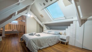 Een slaapkamer met een schuine hemel, een dakraam, een bed met kussens, een nachtkastje en een garderobe.