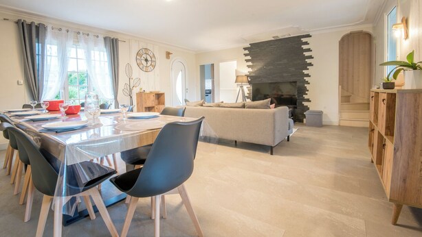 Een moderne woonkamer met een open haard, een eethoek met een tafel gedekt voor vier personen, en een bank.