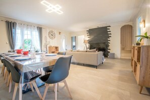 Een moderne woonkamer met een open haard, een eethoek met een tafel gedekt voor vier personen, en een bank.