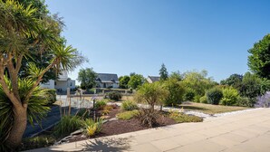 Een woonwijk met een verharde oprit, een verzorgde tuin met diverse beplanting en een huis met schuin dak.