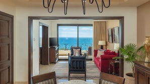A spacious living room with a large window overlooking the ocean, a chandelier, a red sofa, and a dining area with a glass table. - Grand Master Suite at Luxury 5-Star Resort in Cabo San Lucas Mexico (Cabo San Lucas)