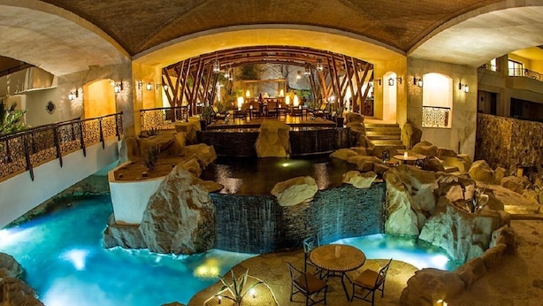 A luxurious indoor pool area with a central bar, seating around the pool, and a stone waterfall feature. - Grand Master Suite at Luxury 5-Star Resort in Cabo San Lucas Mexico (Cabo San Lucas)