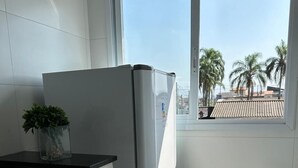 Cocina pequeña con armarios blancos, encimera negra, refrigerador de acero inoxidable y ventana con vista a palmeras y edificios.