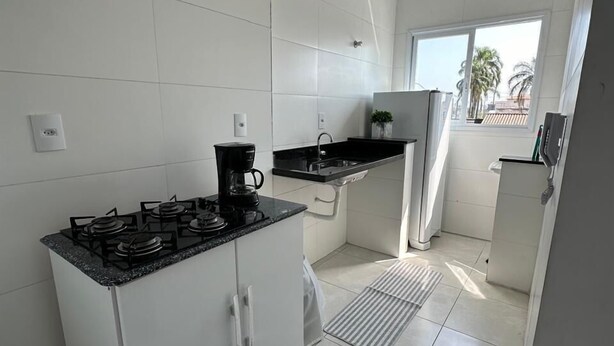 Cocina moderna con armarios blancos, estufa a gas, cafetera y ventana con vistas a palmeras.