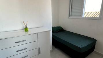A small, clean room with a single bed, a white dresser with drawers, and a window with blinds.