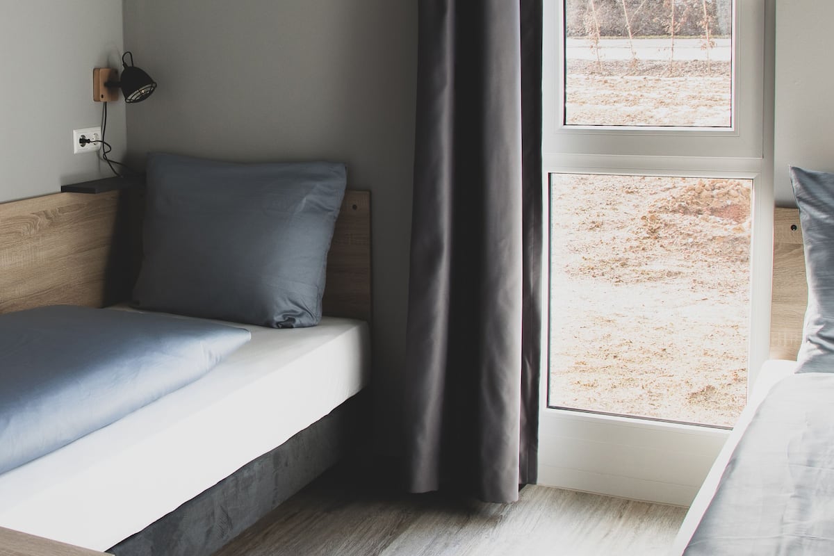 A bedroom with two beds, a window, and a wall-mounted lamp.
