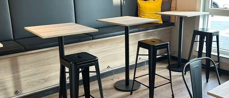 A modern cafe interior with wooden flooring, black and grey seating, and black bar stools.
