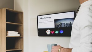 A hotel room with a flat-screen TV mounted on the wall displaying a welcome message and app icons. - Das Schlafwerk Köln-Messe (Cologne)
