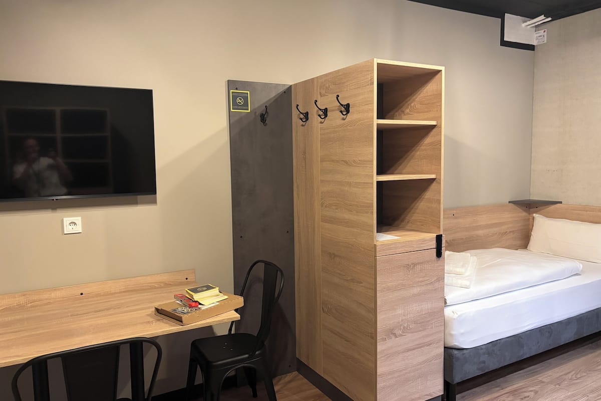 A compact room with a wooden desk, a chair, a bed, and a built-in wardrobe with hooks.