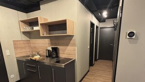 A modern kitchen with dark cabinets, wooden shelves, and a coffee machine. - Das Schlafwerk Köln-Messe (Cologne)
