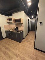 Cozinha moderna com armários escuros, prateleiras de madeira e uma cafeteira.