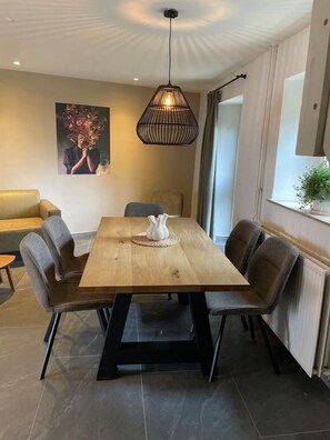 A dining area with a wooden table, four chairs, a pendant light, and a painting on the wall. - Sfeervol huisje nabij Valkenburg (Voerendaal)