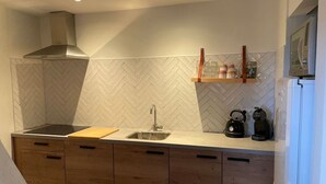 A modern kitchen with a herringbone tile backsplash, wooden cabinets, a stainless steel sink, and a built-in stove. - Sfeervol huisje nabij Valkenburg (Voerendaal)