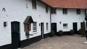 A white building with a red-tiled roof, a brick courtyard, and a black door. - Sfeervol huisje nabij Valkenburg (Voerendaal)