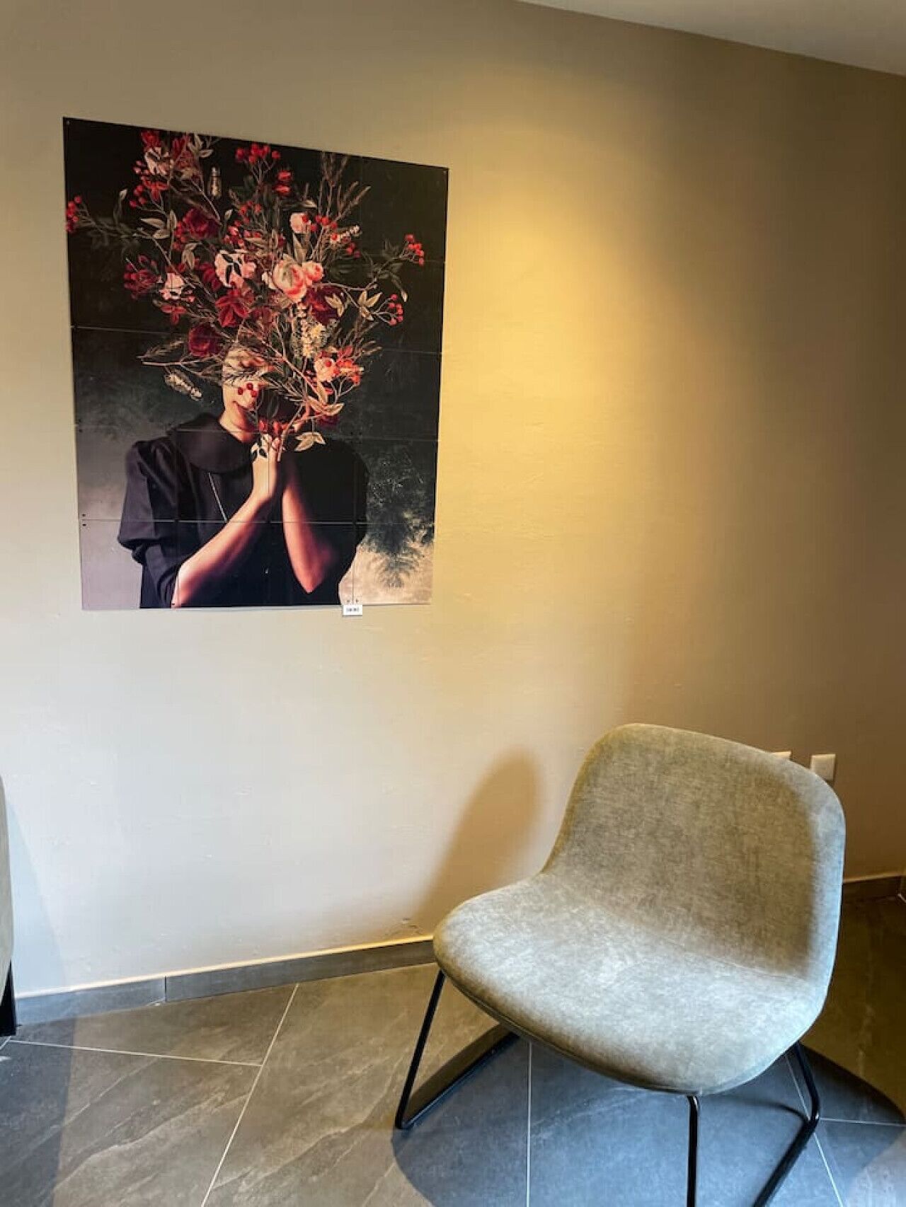 A modern interior with a dark-toned artwork on the wall, a grey upholstered chair, and a tiled floor.