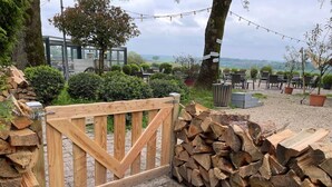 A wooden gate leading to a patio area with stacked firewood, outdoor seating, and a view of the countryside. - Sfeervol huisje nabij Valkenburg (Voerendaal)