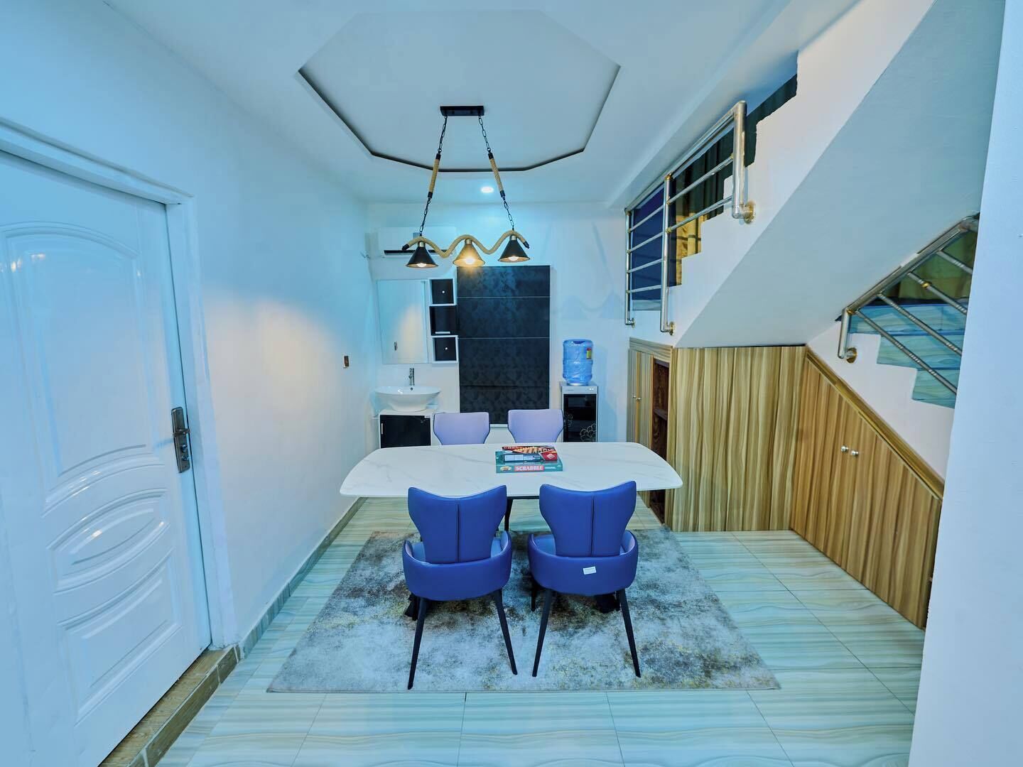 Eine moderne Küche mit weißer Arbeitsplatte, zwei blauen Stühlen, einem weißen Esstisch und einer außergewöhnlichen Deckenleuchte.