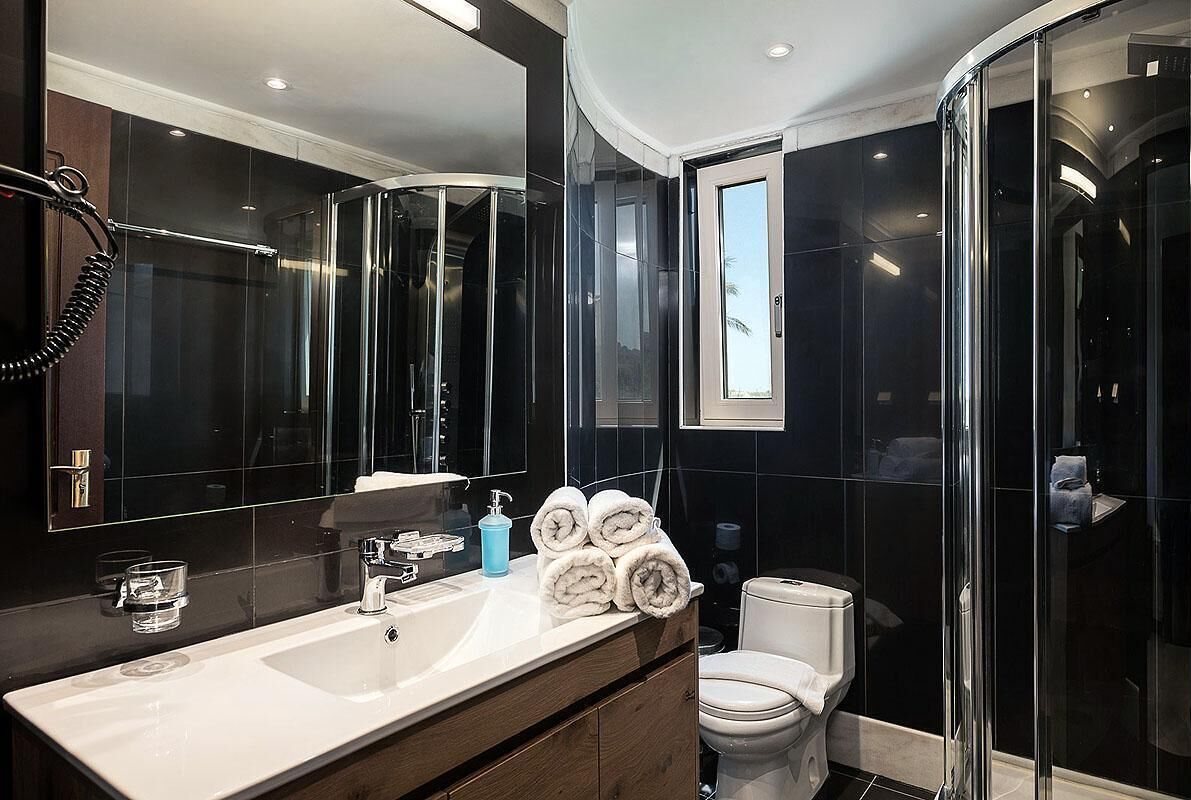 Un baño moderno con un espejo grande, un lavamanos blanco, un inodoro y una cabina de ducha de vidrio.