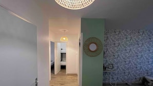 A hallway with a bunk bed in the background, a round mirror on the wall, and a patterned wallpaper. - Agréable logement 8 personnes (Chalon-sur-Saône)