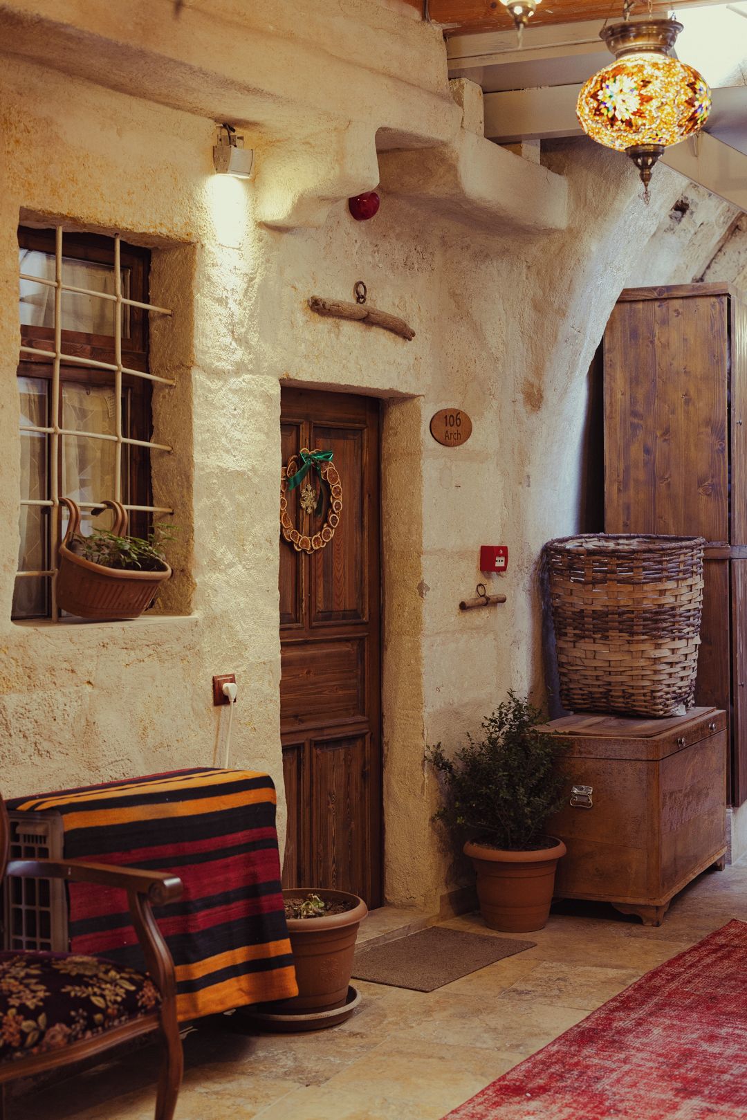A rustic interior with a wooden door, a bench, a potted plant, a wicker basket, and a hanging light fixture.