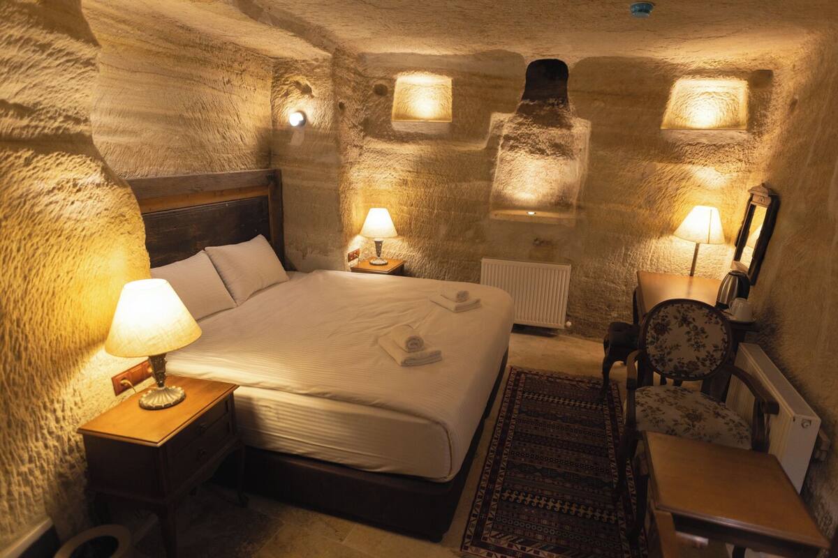 Ein gemütliches Schlafzimmer mit Steinsäulen, einem großen Bett, Nachttischlampen, einem Heizkörper und einem kleinen Tisch.
