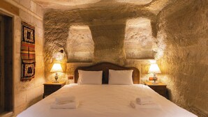 A stone-walled room with a bed, two bedside lamps, and a wall hanging. - Memory Cave House (Nevsehir)