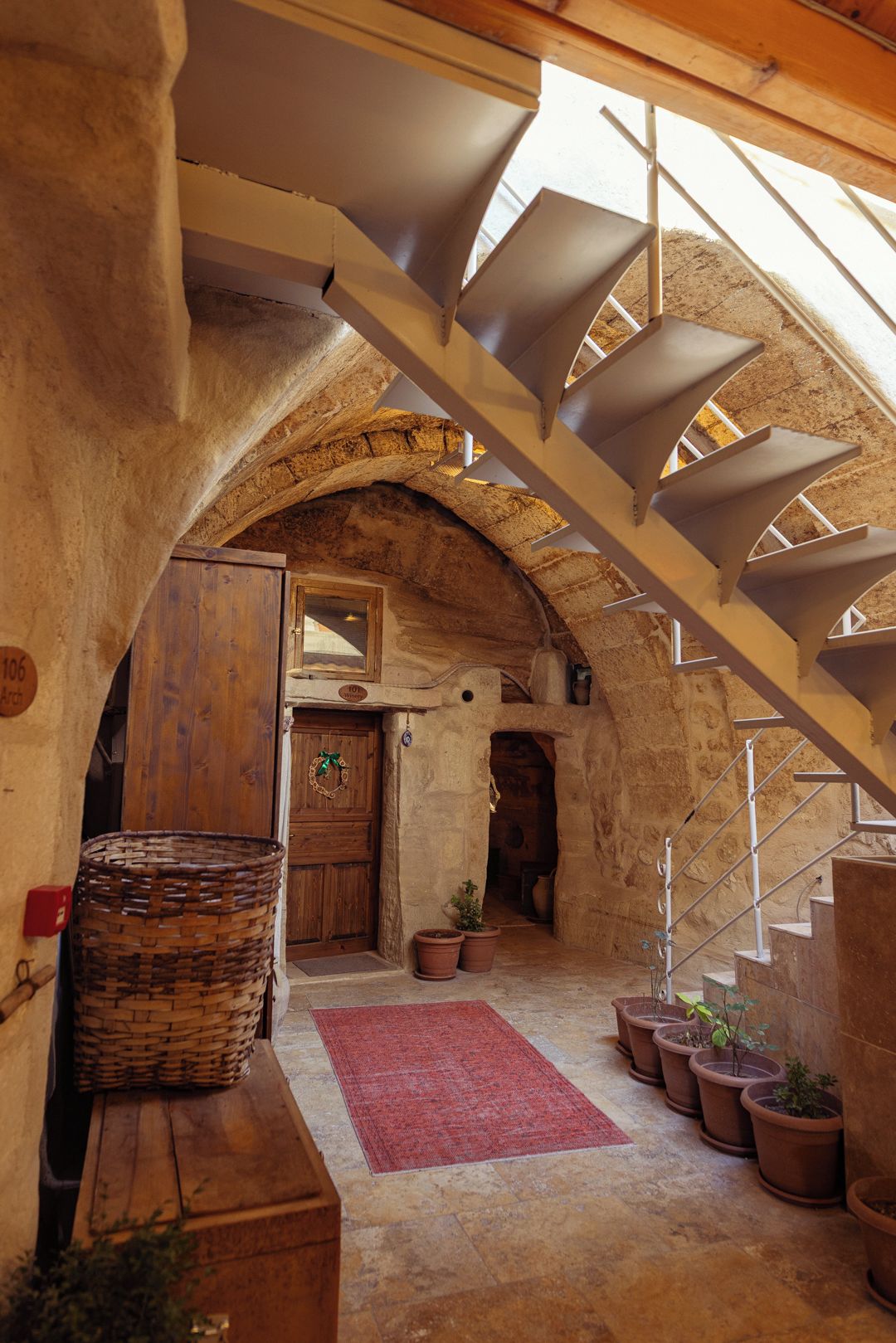 A rustic interior with a wooden staircase, a red rug, and potted plants.