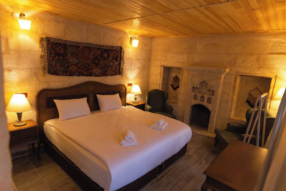 Ein Zimmer mit einem großen Bett, zwei Nachttischlampen, einem Sessel, einem Kamin und einem Wandteppich.