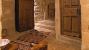 A stone-walled room with wooden doors, a staircase, and a patterned rug. - Memory Cave House (Nevsehir)