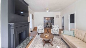 Un salon avec une cheminée, un canapé, deux fauteuils, une table basse et un téléviseur fixé au mur.