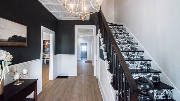 Un escalier orné de motifs floraux en noir et blanc, un lustre et un couloir menant à une autre pièce.