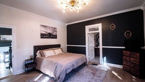 Une chambre à coucher comprenant un lit, une table de chevet, une commode et une porte donnant sur une autre pièce.