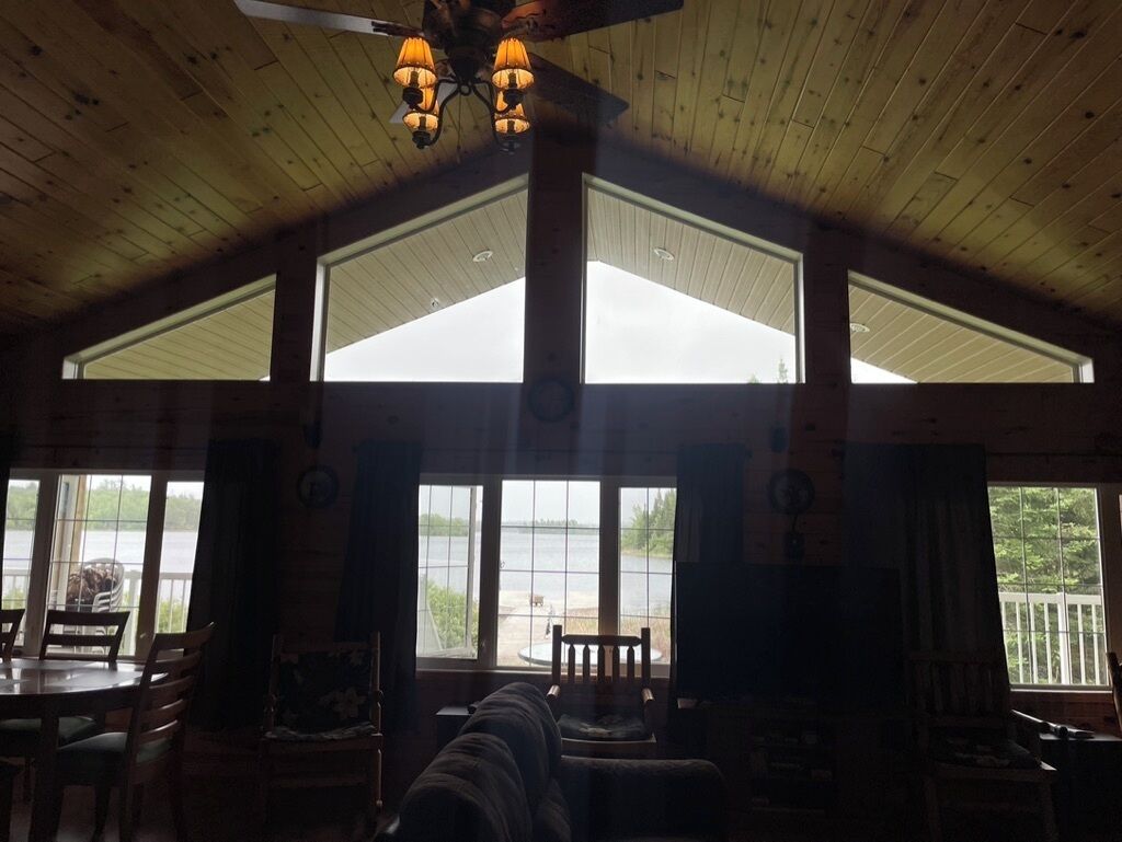A cabin interior with a dining area, a sofa, and large windows overlooking a body of water.