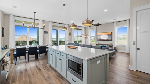Une cuisine spacieuse dotée d’un grand îlot central, de luminaires suspendus modernes et offrant une vue sur l’extérieur.