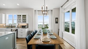 Une cuisine moderne avec des meubles blancs, une table à manger en bois pouvant accueillir six personnes et une vue sur la ville grâce à de grandes fenêtres.