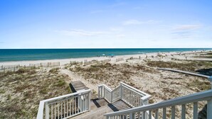 A beach view from a wooden deck with a white railing, sandy dunes, and the ocean. - Turtle Tracks: Beachfront, East End, Pet Friendly, Sunset Beach (St. George Island)