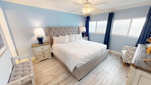 Une chambre avec un grand lit, une table de chevet avec une lampe, une chaise et une vue sur la plage.