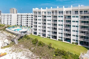 A multi-story hotel with balconies, a pool area, and a beach view.
