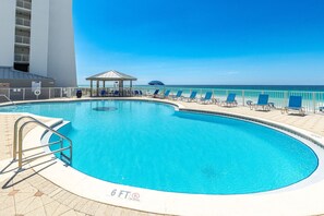 A pool with a 6 ft depth limit and no diving sign, surrounded by lounge chairs and a covered seating area, with a view of the ocean.