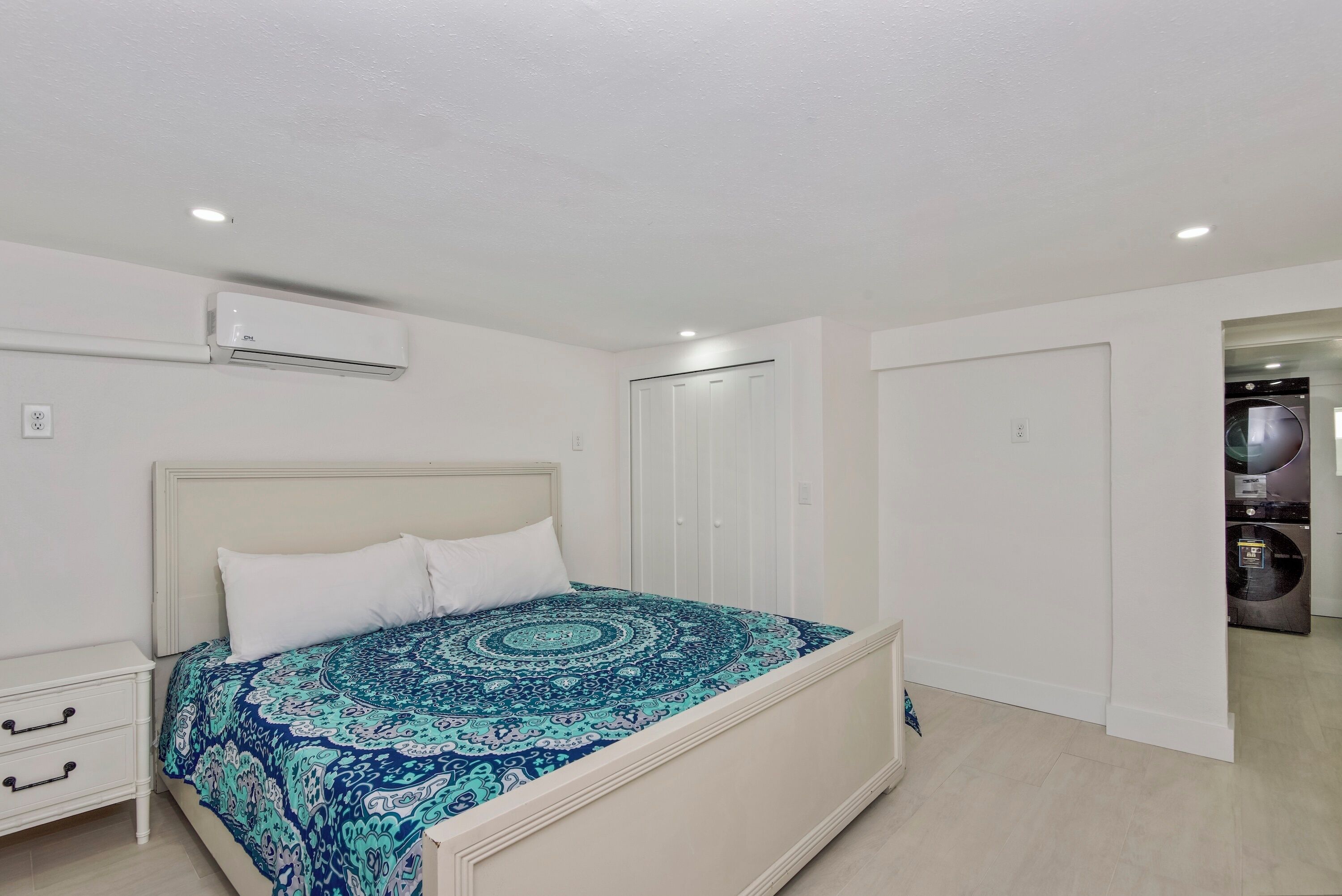 A bedroom with a bed, a nightstand, a wardrobe, and an air conditioning unit.