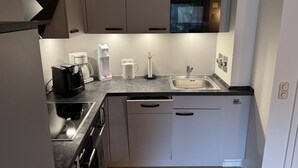 A modern kitchen with a built-in microwave, a coffee maker, a kettle, and a sink.