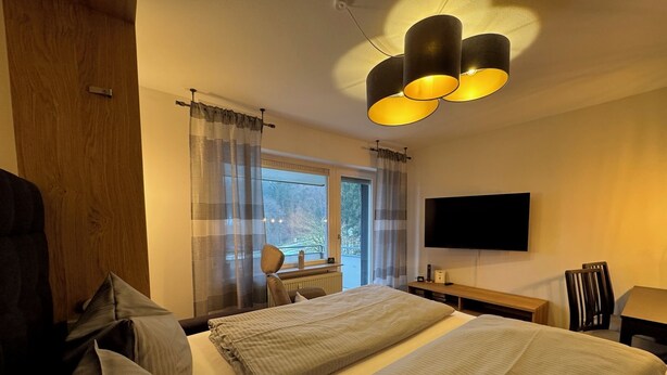 A bedroom with two beds, a wooden wardrobe, a TV, and a window with curtains.