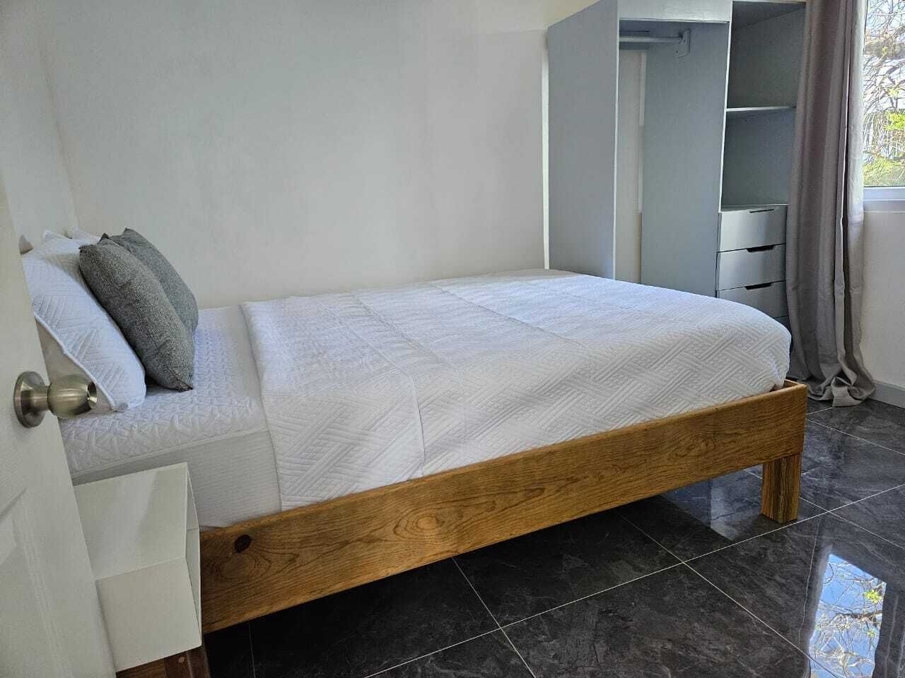 Un letto singolo con struttura in legno e biancheria bianca in una stanza con pavimento piastrellato scuro.