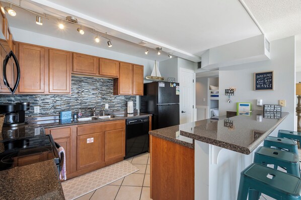 A modern kitchen with wooden cabinets, a granite countertop, and a black refrigerator. - Edgewater Tower 1 2bd/2ba sleeps 6 with great amenities (Panama City Beach)