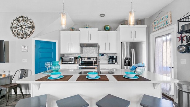 A modern kitchen with white cabinets, a central island with stools, stainless steel appliances, and a blue door. - Hilltop Manor-4 Bedrooms 2 1/2 Bathrooms *Sleeps 10* Spring open! (Panama City Beach)