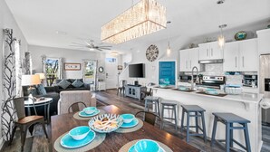 A modern kitchen with white cabinets, a large island, and a dining area with blue tableware. - Hilltop Manor-4 Bedrooms 2 1/2 Bathrooms *Sleeps 10* Spring open! (Panama City Beach)