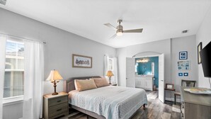 A bedroom with a bed, nightstands, a ceiling fan, and a view into the bathroom. - Hilltop Manor-4 Bedrooms 2 1/2 Bathrooms *Sleeps 10* Spring open! (Panama City Beach)