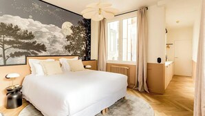 Un dormitorio con una cama grande, una mesita de noche, un mural en la pared, una ventana con cortinas y un radiador.